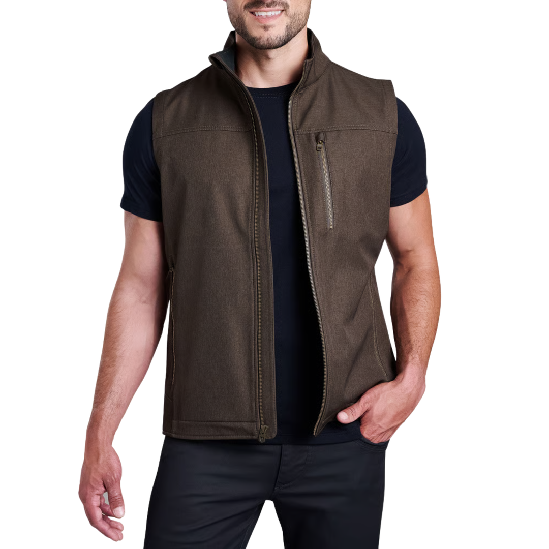 A man wearing a brown zip-up sleeveless vest over a black t-shirt and black pants, shown from the waist up against a plain white background.