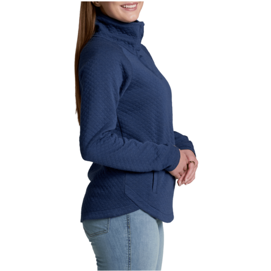 A woman wearing a navy blue quilted long-sleeve turtleneck sweater and light blue jeans, shown from a side profile against a white background.