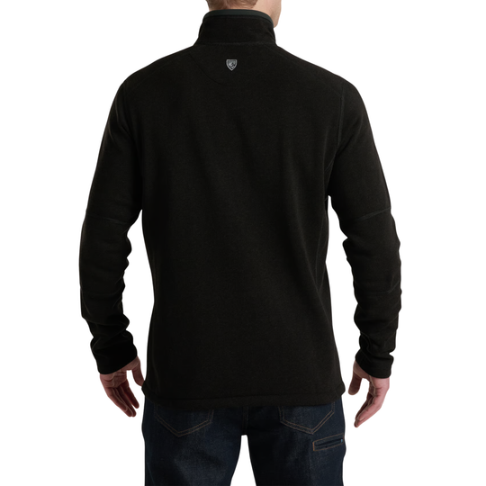 A man viewed from the back wearing a black long-sleeve quarter-zip fleece pullover with a small shield logo on the upper neck, paired with dark blue jeans against a white background.