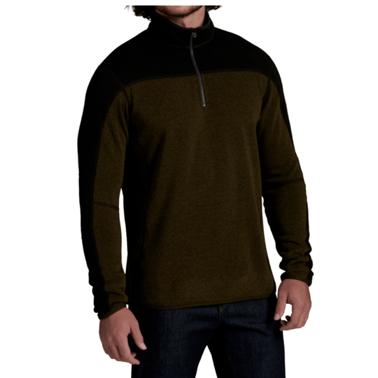 A man wearing a dark olive green and black quarter-zip pullover sweater with dark blue jeans, shown from the chin down against a plain white background.