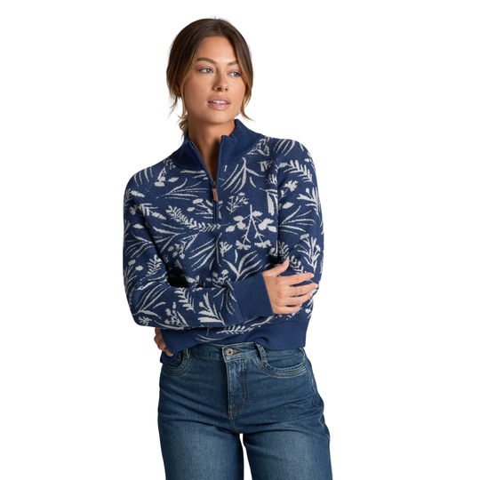 A woman modeling a navy blue quarter-zip sweater with a white botanical leaf pattern, paired with blue jeans, against a solid white background.