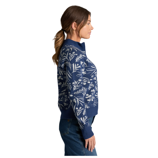 A woman shown in side profile wearing a navy blue knit sweater with a white botanical leaf pattern, paired with blue jeans, against a plain white background.