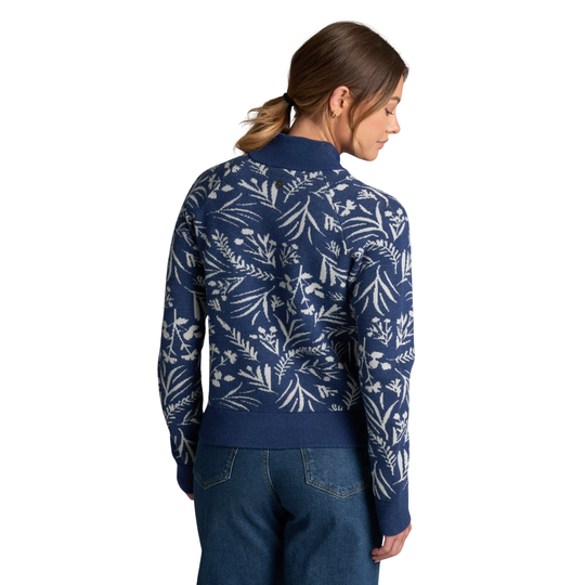 A woman shown from the back wearing a navy blue mock-neck sweater with a white botanical leaf pattern, paired with blue jeans, against a plain white background.