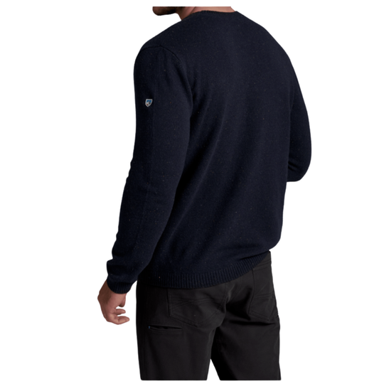 A man wearing a dark navy blue knit sweater, shown from the back. The sweater has a small shield logo on the upper left shoulder and is paired with black pants against a plain white background.