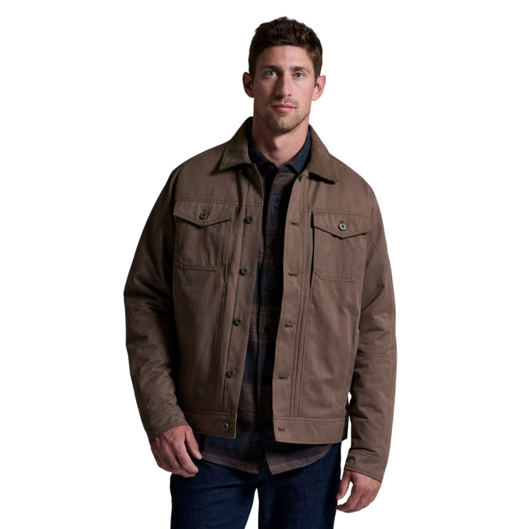 A man wearing a brown waxed canvas utility jacket over a dark plaid shirt and blue jeans, photographed against a solid white background.