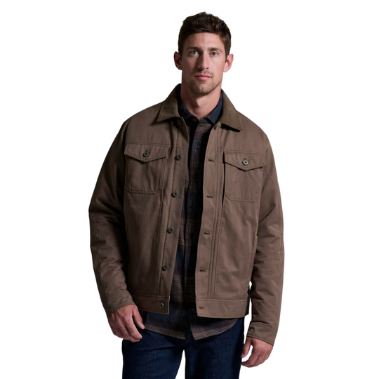 A man wearing a brown waxed canvas utility jacket over a dark plaid shirt and blue jeans, photographed against a solid white background.