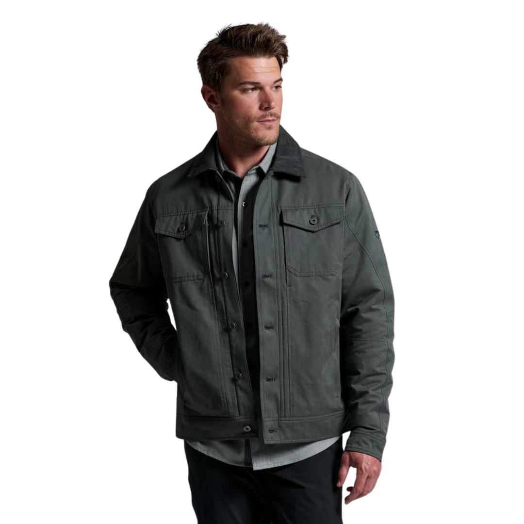A man wearing a dark gray utility jacket over a gray button-up shirt and dark pants, photographed against a plain white background.
