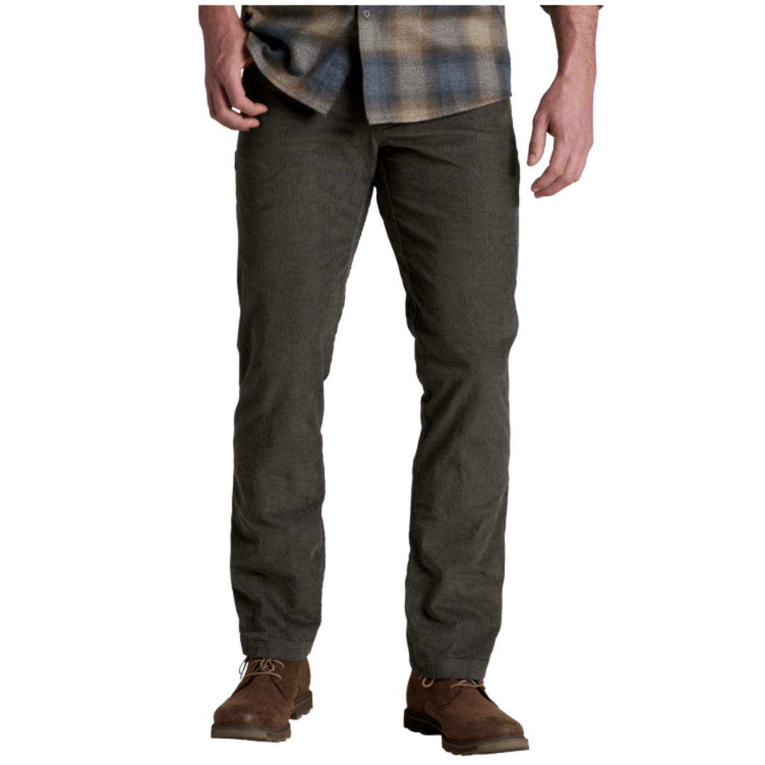 A person wearing dark charcoal gray straight-leg work pants, a brown and blue plaid shirt, and brown leather work boots, shown from the waist down on a white background.