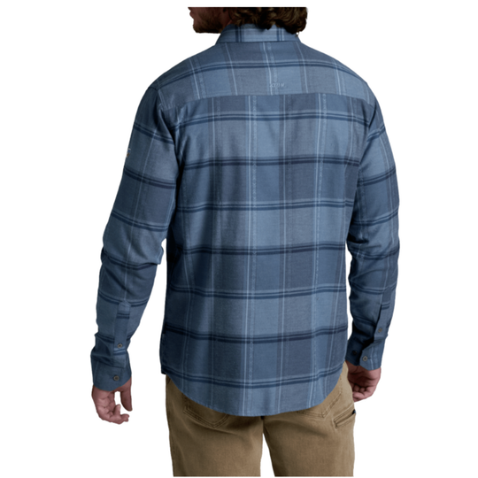A man wearing a blue and gray plaid long-sleeve button-down shirt, viewed from the back, paired with khaki pants against a white background.