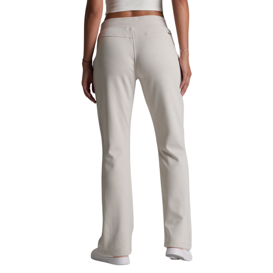 A model shown from the back wearing light beige straight-leg sweatpants, a white crop top, and white sneakers against a plain white background.