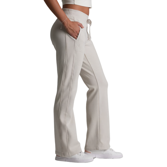 A side view of a person wearing light beige wide-leg sweatpants with a drawstring waist, paired with white sneakers against a plain white background.