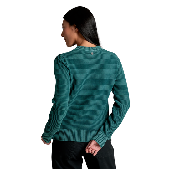 A woman shown from the back wearing a dark teal green ribbed knit sweater and black pants, photographed against a plain white background.