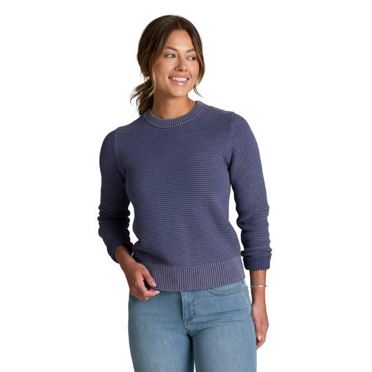 A woman wearing a navy blue ribbed knit crewneck sweater and light blue jeans, standing against a plain white background.