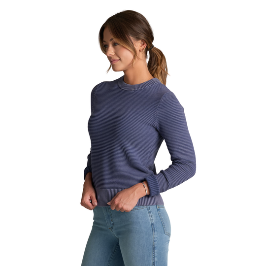 A woman wearing a navy blue ribbed knit crewneck sweater and light blue jeans, shown from a side profile against a solid white background.