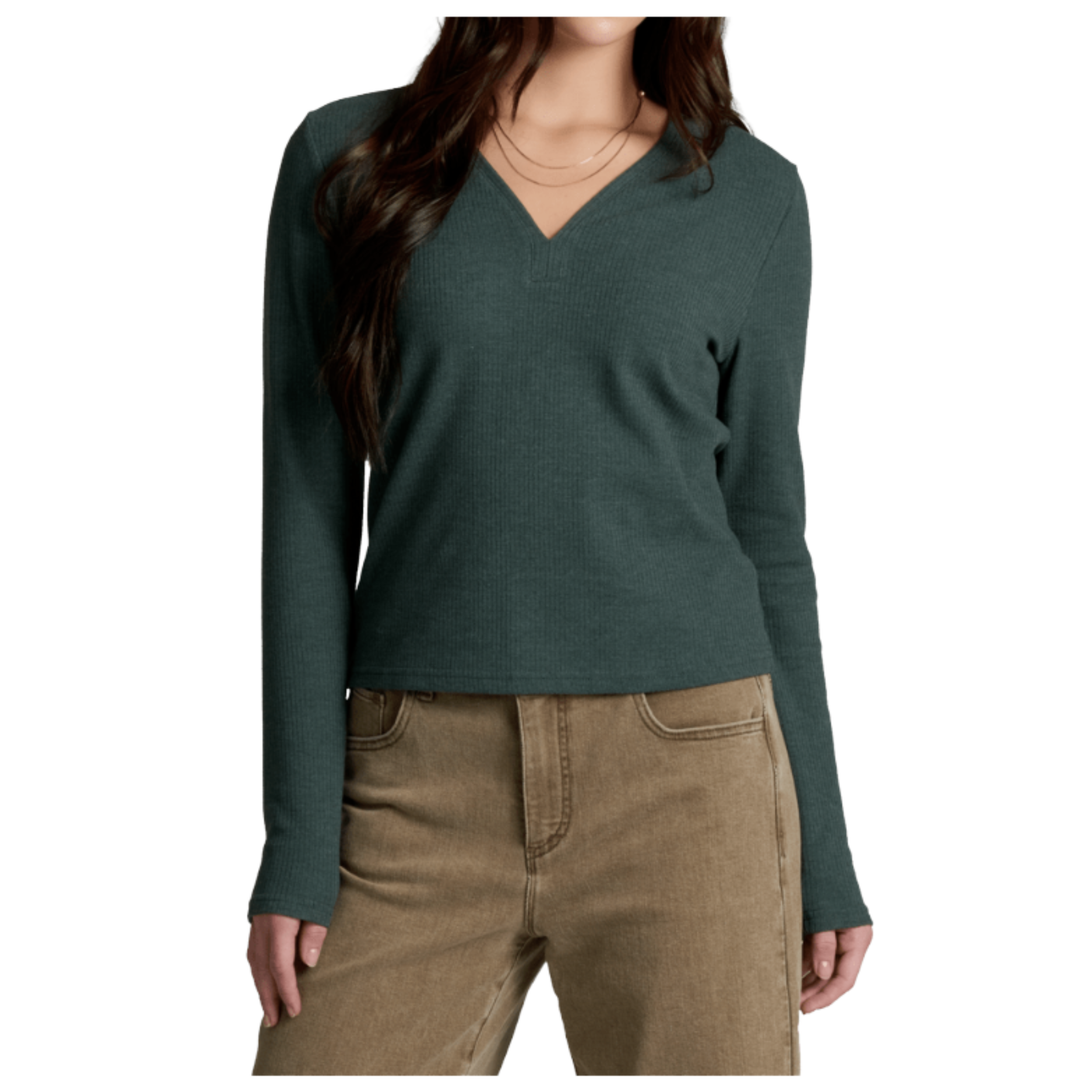A woman wearing a dark green long-sleeve V-neck knit top and tan pants, shown from the neck down against a plain white background.