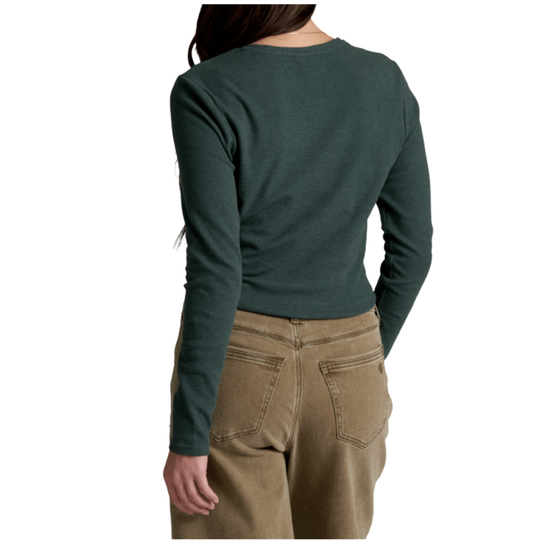 A woman shown from the back wearing a dark green long-sleeve crewneck top and tan pants against a plain white background.