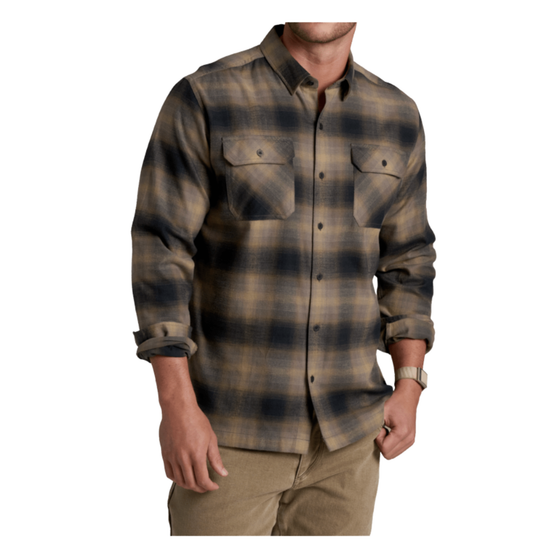 A man wearing a long-sleeve button-up plaid flannel shirt in brown and navy tones, paired with khaki pants, against a plain white background.