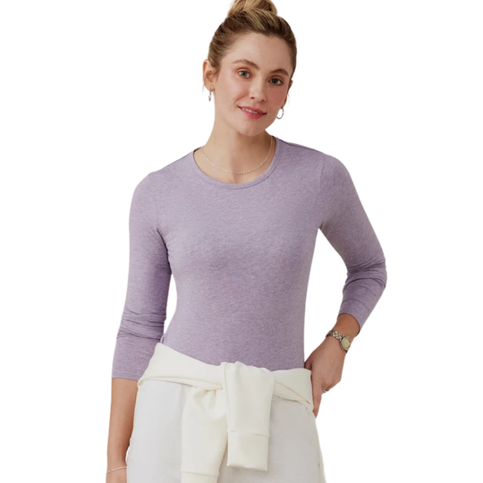A woman shown from the front wearing a heathered light purple long-sleeve top and white pants against a plain white background.