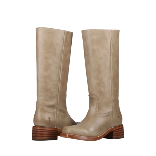 A pair of mid-calf western boots in a light taupe-beige leather, featuring stacked brown wooden heels and a small embroidered logo on the side, set against a plain white background.
