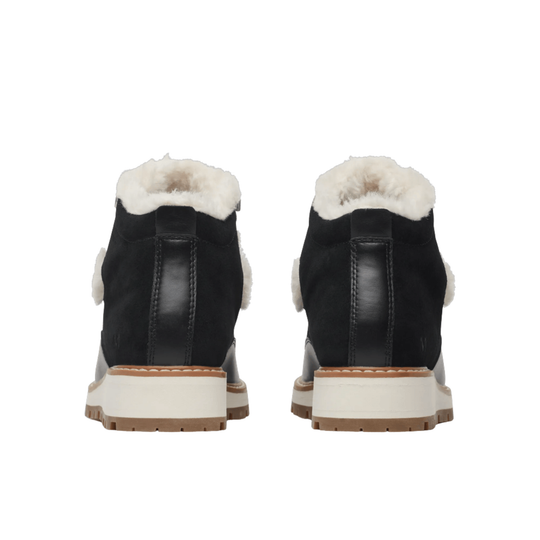 A pair of black ankle boots with white shearling lining, shown from the back on a solid white background.