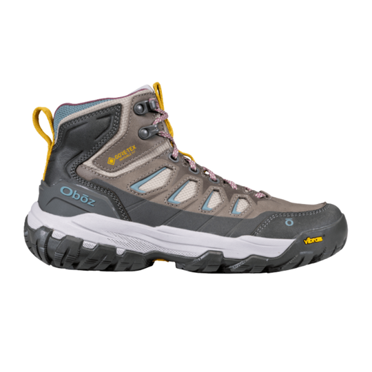 A mid-cut hiking boot from Oboz, featuring a gray and brown suede and synthetic upper with light blue mesh panels, a white midsole, and a black Vibram outsole.