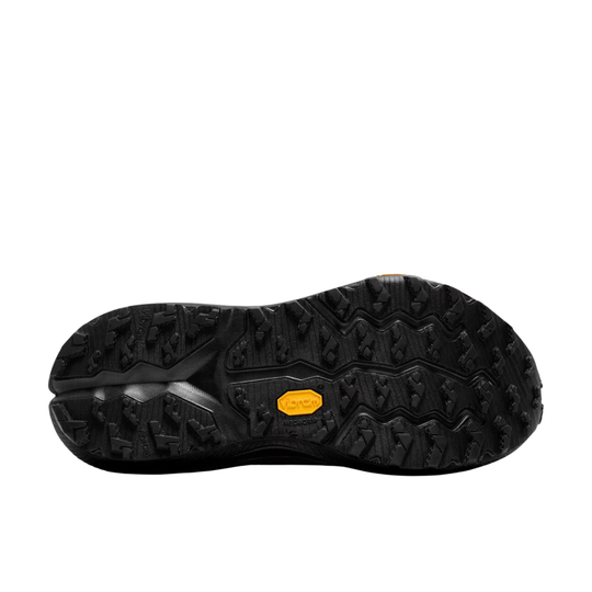 The black rubber outsole of a shoe, showing deep tread patterns and a small yellow Vibram logo badge, isolated on a white background.
