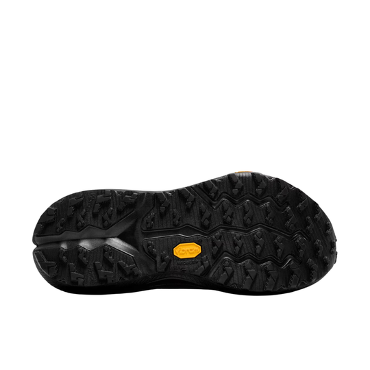 The black rubber outsole of a shoe, showing deep tread patterns and a small yellow Vibram logo badge, isolated on a white background.
