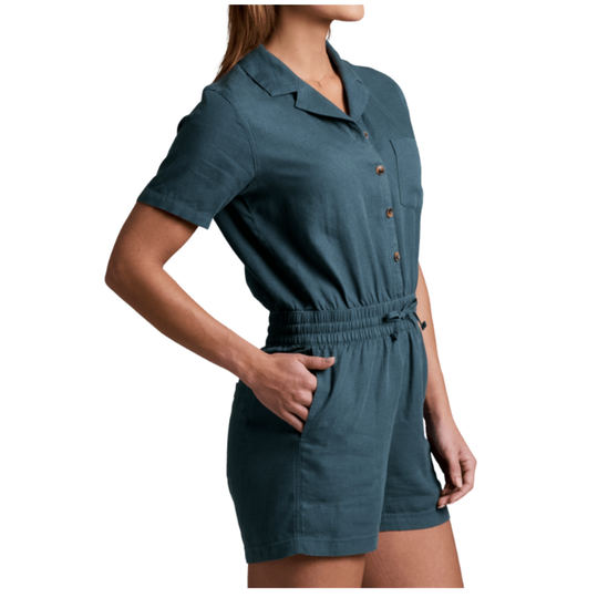 A woman wearing a slate blue short-sleeve romper with a button-down front and side pockets, shown from the side against a plain white background.
