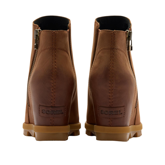 A pair of brown leather wedge ankle boots shown from the back, featuring side zippers, a tan midsole, and a SOREL logo patch on the heel.