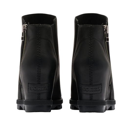 A pair of black leather ankle boots shown from the back, featuring side zippers, a chunky black wedge heel, and a SOREL logo embossed on the heel.