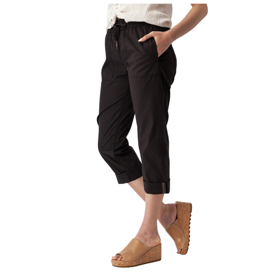 A model wearing black cropped pants with a drawstring waist, side pockets, and rolled cuffs, paired with tan wedge slide sandals against a plain white background.
