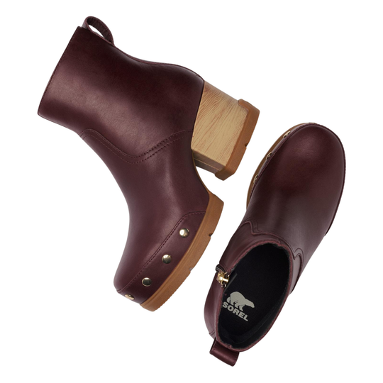 A pair of women's ankle boots in dark burgundy leather, featuring a chunky wooden block heel, decorative brass studs on the toe, and a side zipper. One boot is shown from a three-quarters angle displaying the side profile and heel, while the other is shown from the back displaying the black interior with the 'SOREL' brand logo.