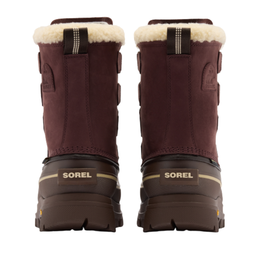 A pair of Sorel mid-calf winter boots shown from the back, featuring a dark brown suede upper, a thick dark brown rubber sole, a black heel tab with a white fleece lining, and a beige fleece collar.