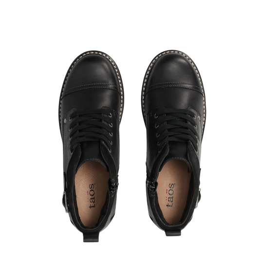 A pair of black leather lace-up ankle boots with side zippers, shown from a top-down view on a solid white background. The brand name 'taos' is printed on the tan insole.