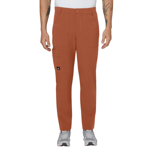 A person modeling a pair of rust-orange cargo pants with a small black logo patch on the side pocket, paired with a white shirt and gray sneakers against a plain white background.