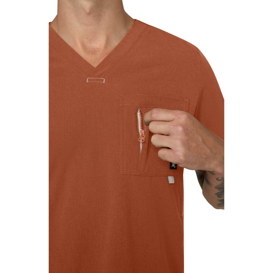 A close-up of a person wearing a rust-orange waffle-knit V-neck pocket shirt, showing a hand reaching into a chest pocket to pull a pen out of the pocket.