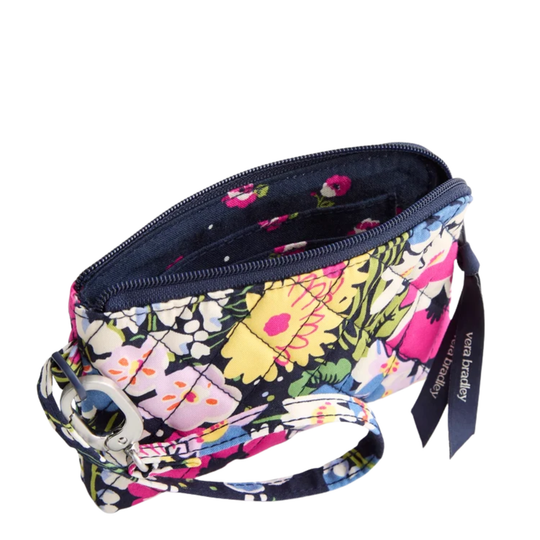 A floral zippered wristlet pouch by Vera Bradley, featuring a multicolor print of yellow, pink, and white flowers on a dark navy background. It has a matching fabric wrist strap with a metal ring clasp and a branded fabric tag.