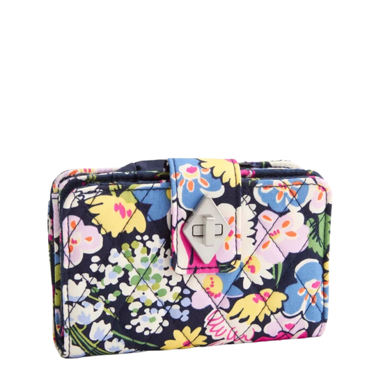 A quilted zip-around wallet with a vibrant floral print on a navy background, featuring pink, blue, yellow, and white flowers with green leaves. Silver turnlock.