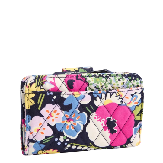 A quilted zip-around wallet with a vibrant floral print on a navy background, featuring pink, blue, yellow, and white flowers with green leaves.