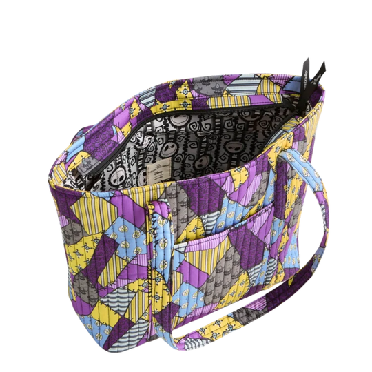 A quilted fabric tote bag with a colorful patchwork design featuring purple, yellow, blue, and gray geometric patterns. The bag is shown open, revealing a black patterned interior lining, a front pocket, and a shoulder strap, set against a plain white background.