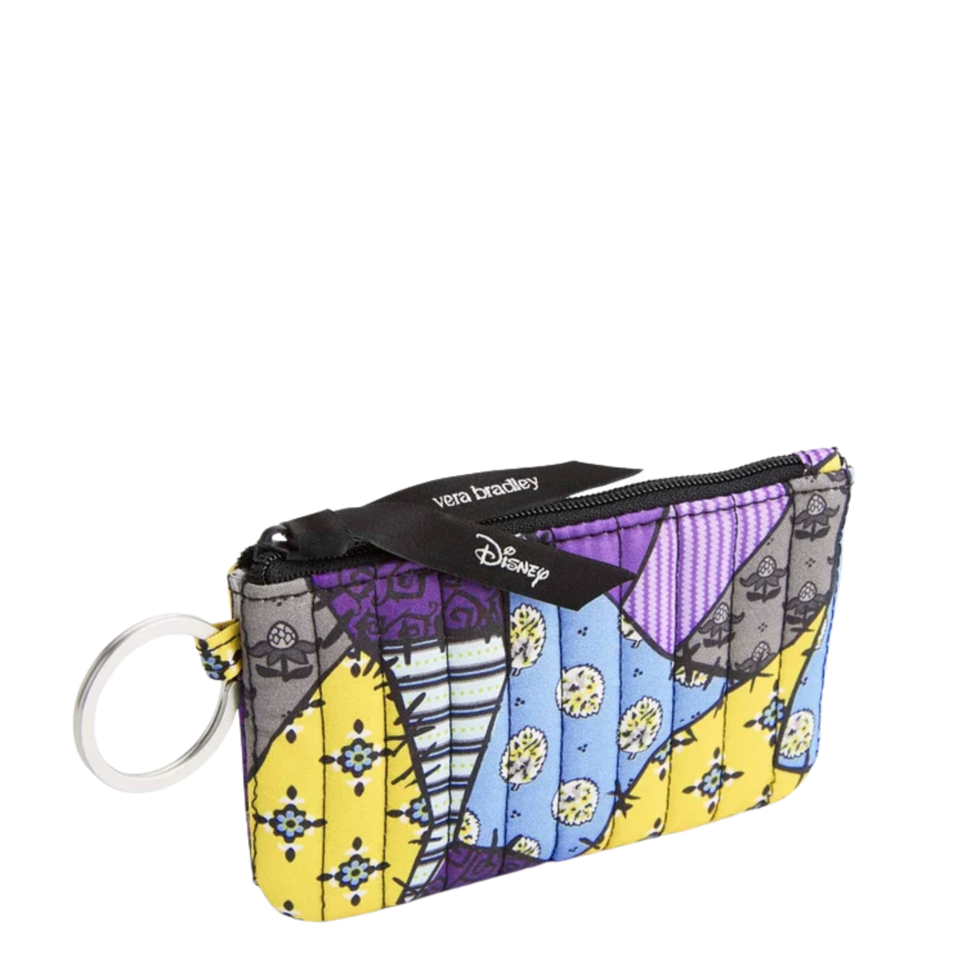A small zippered coin pouch with a colorful patchwork print featuring purple, yellow, blue, and gray sections. It has a black zipper tab with the Vera Bradley and Disney logos, and a silver metal key ring attached on the left, set against a plain white background.