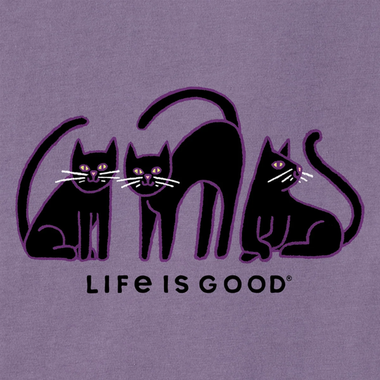 A close-up of a purple garment featuring a black graphic of three stylized cats and the text 'LIFE IS GOOD' in black. The fabric texture is visible, and the brand name 'Life is Good' is clearly printed.