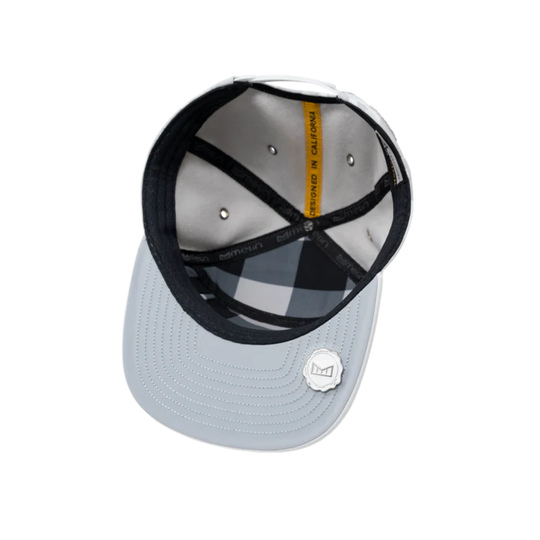 A light gray snapback cap shown from an overhead angle, revealing a black and white buffalo plaid interior lining, black adjustable straps, and a small white circular logo badge on the brim.