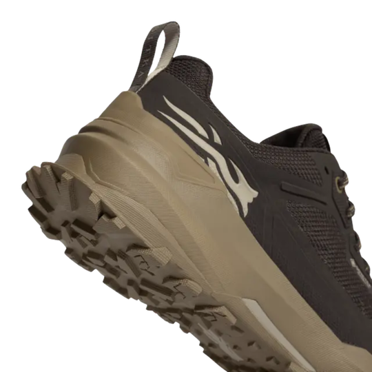 A close-up of a trail running shoe showing the side profile, featuring a dark brown mesh upper, a tan midsole, and a rugged brown outsole with a white logo accent.