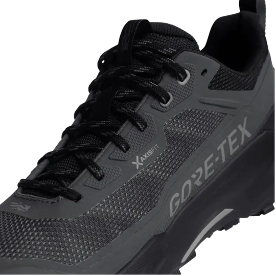 A close-up of a dark gray and black Gore-Tex trail running shoe on a white background, showing the side profile with the brand name 'GORE-TEX' printed in gray on the side panel.