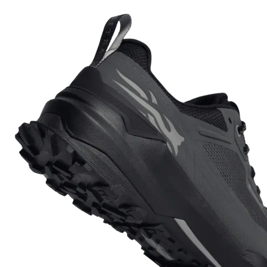 A close-up shot of a black and dark gray trail running shoe, showing the side profile, textured outsole, and a gray logo on a white background.