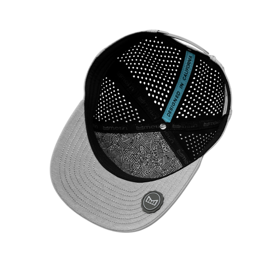 A structured trucker-style cap shown from an angled top-down view on a plain white background. The cap features a light gray structured brim with a circular logo patch, black mesh back panels, a black front suspension strap, and a distinctive bright blue vertical label on the back that reads 'Designed in california'.