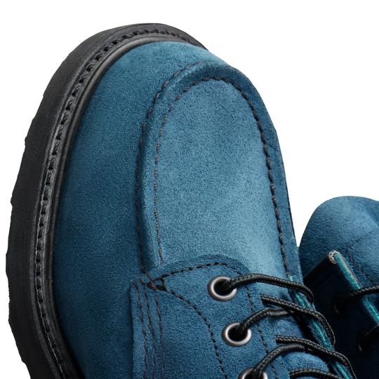 Close-up of a blue suede lace-up boot showing the side profile with a black sole and black laces against a light gray background.