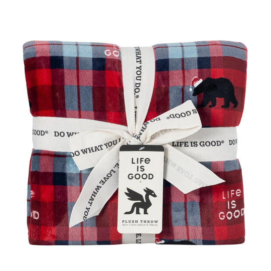 A folded plush throw blanket with a red, blue, and navy plaid pattern, featuring a black bear graphic and white text. It is wrapped in a white ribbon printed with 'LIFE IS GOOD' and has a matching brand tag.