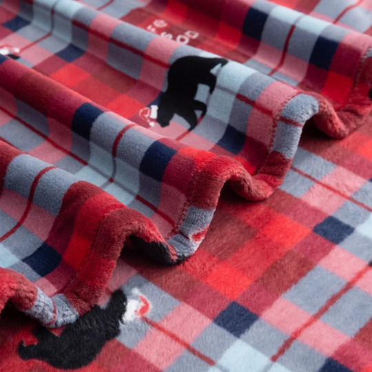 A close-up of a plush fleece blanket with a red, gray, and navy plaid pattern, featuring black polar bear illustrations and a soft sherpa lining.